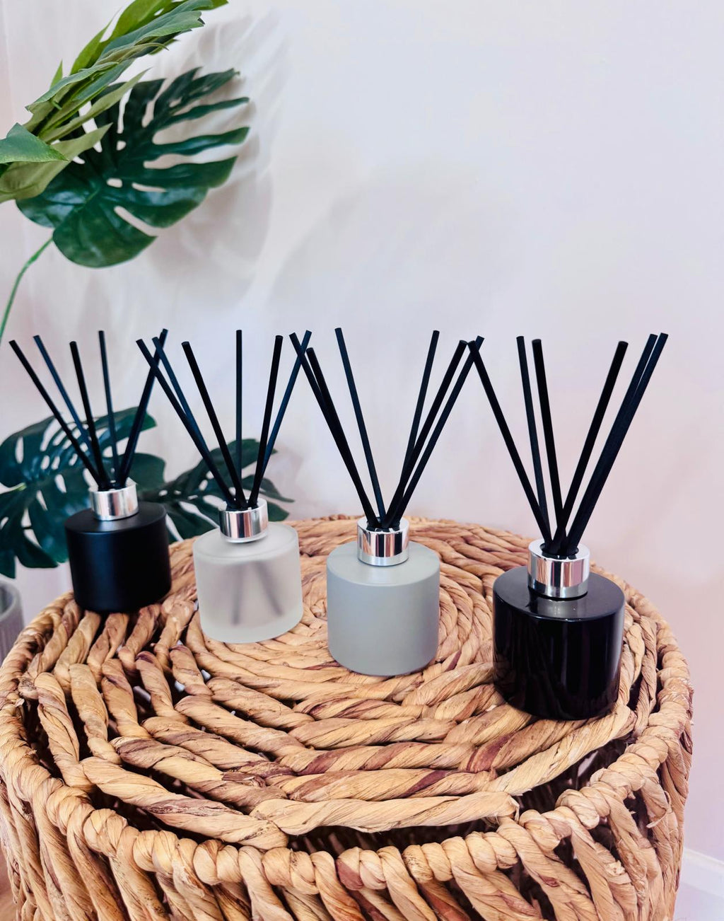 Four diffusers with black sticks on a woven stool with plants in the background