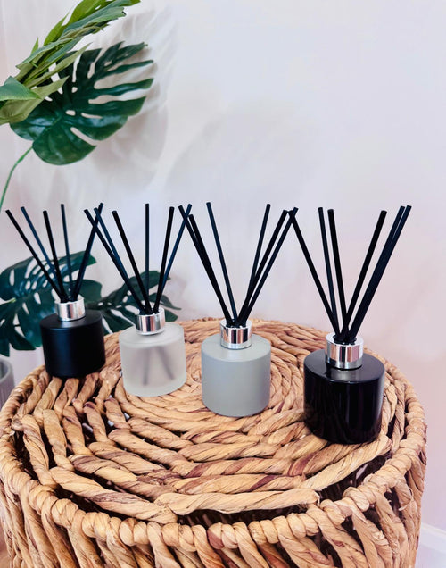 Four diffusers with black sticks on a woven stool with plants in the background