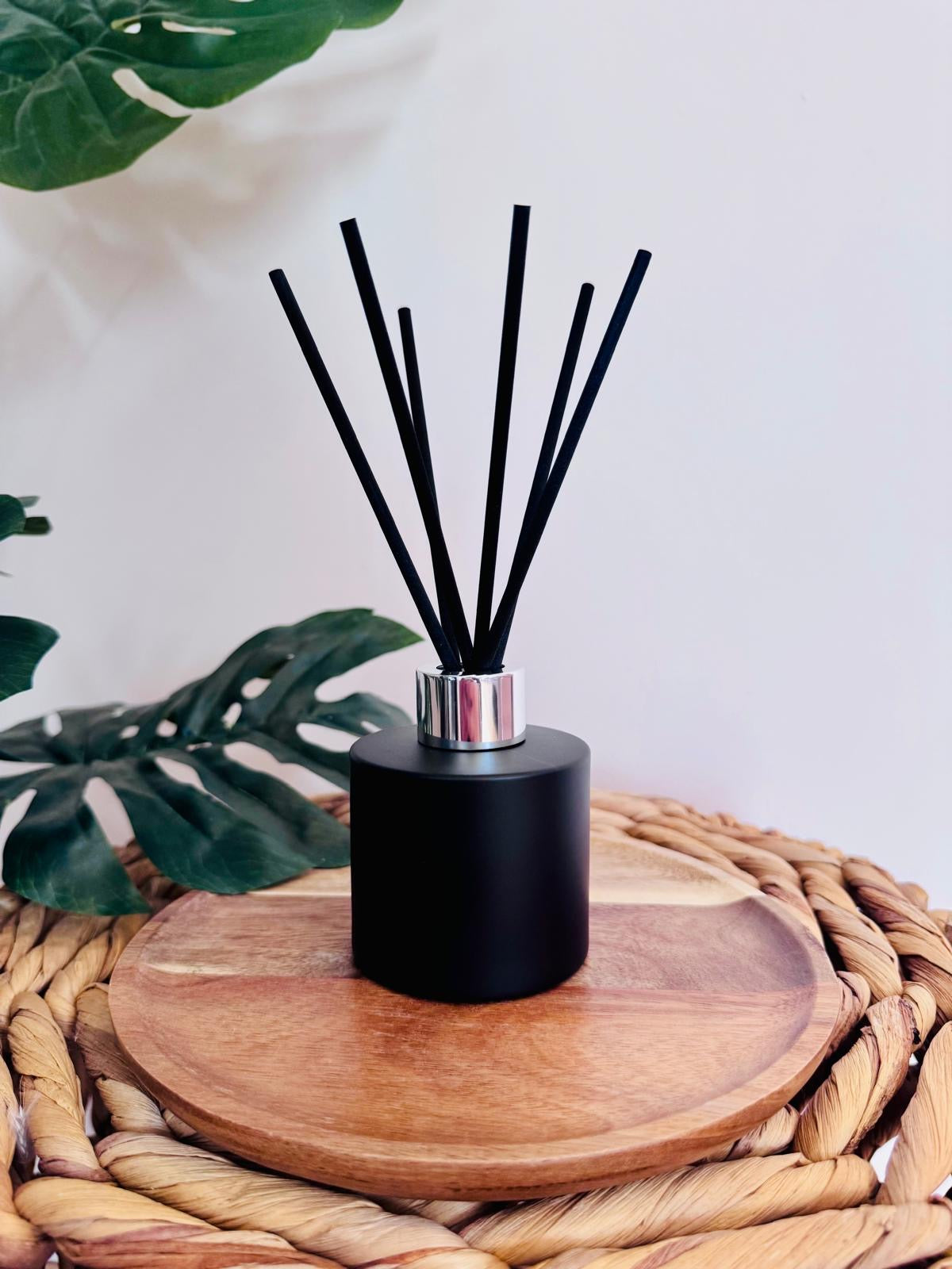 Black diffuser with sticks on a wooden coaster with plants in the background