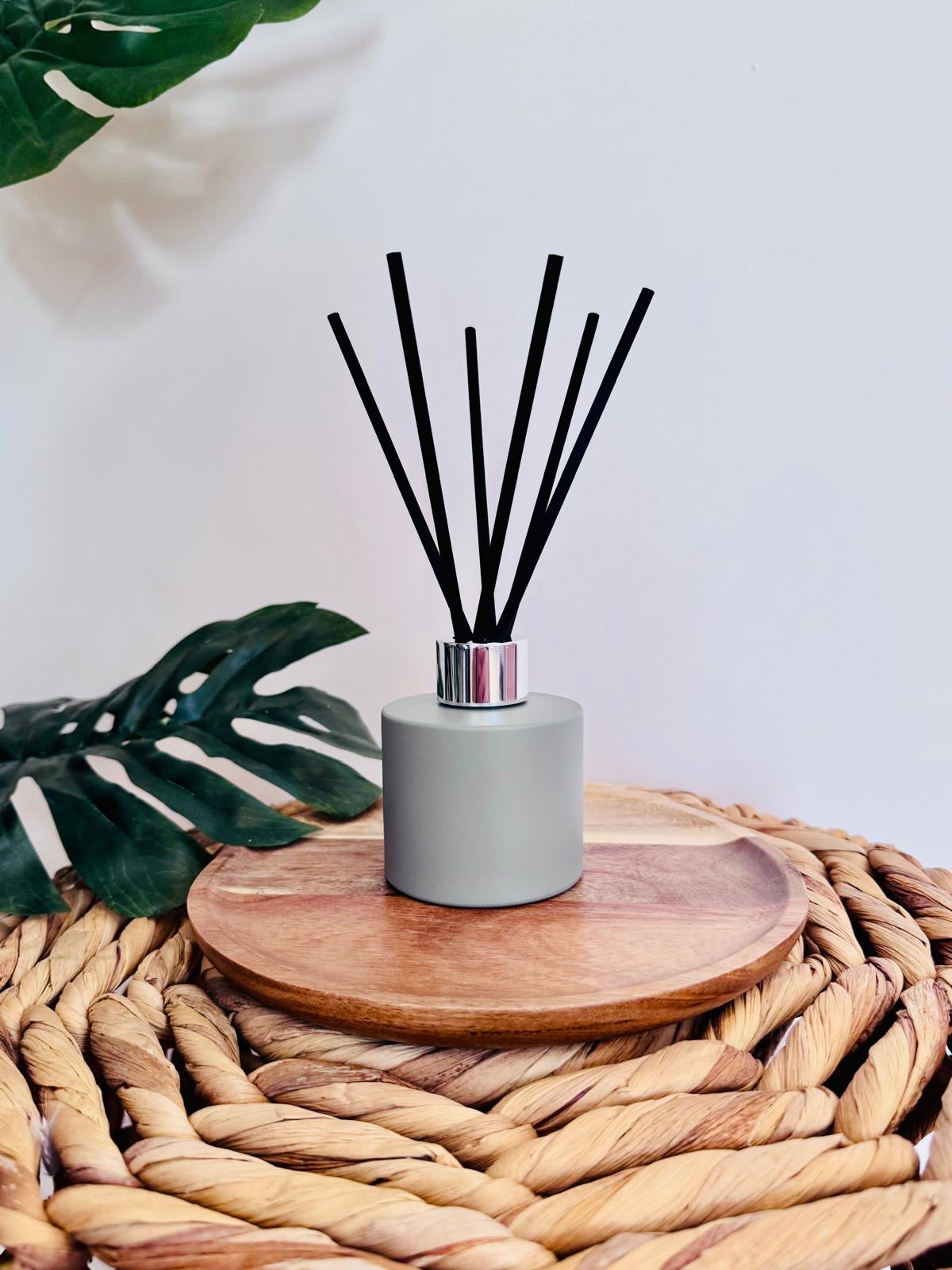 Reed diffuser on a wooden coaster with green leaves in the background