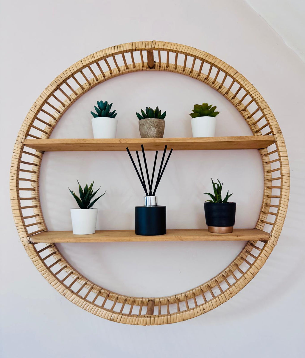 Round wooden shelf with wicker frame holding plants and a diffuser on a white wall.