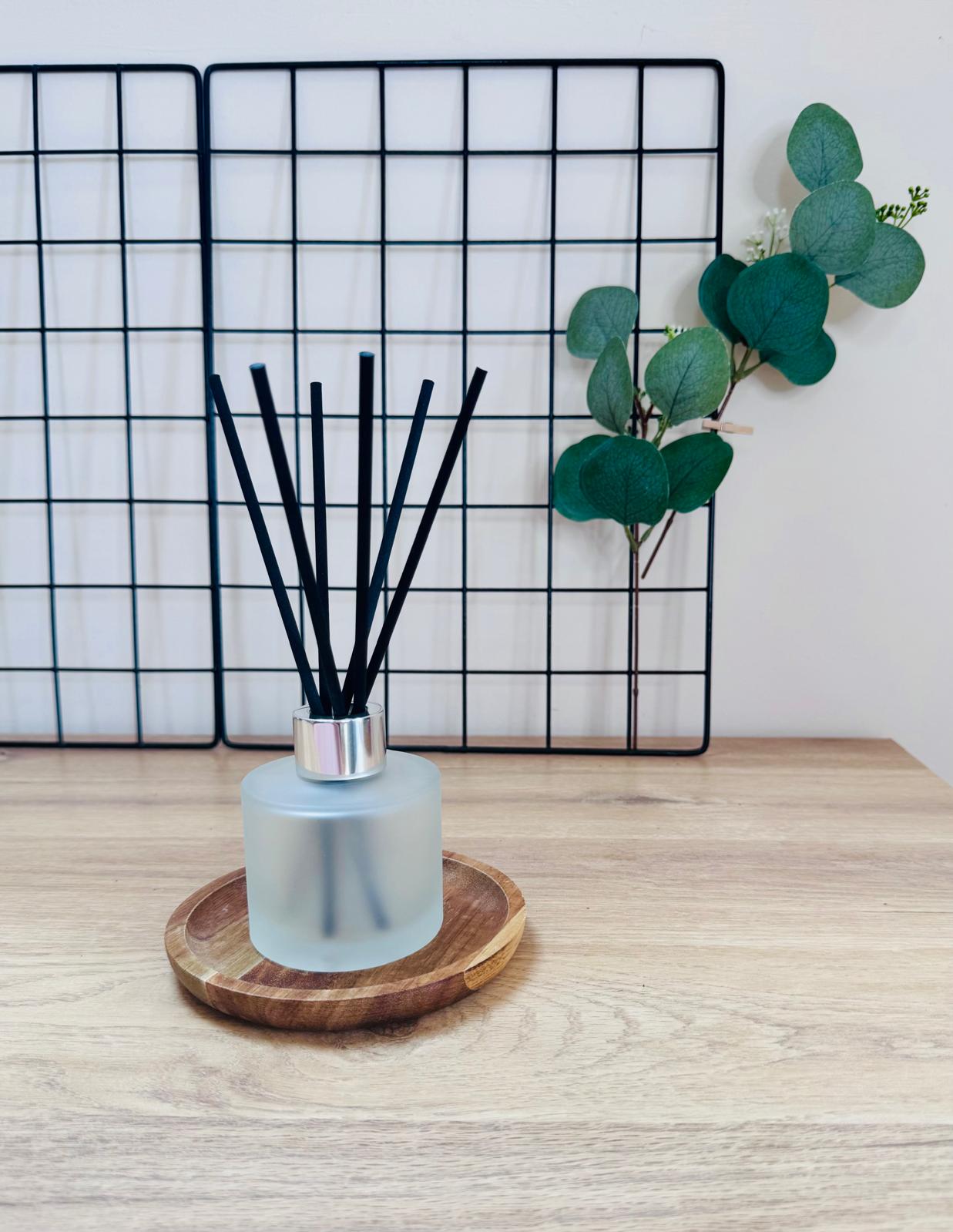 Diffuser with black sticks on a wooden coaster in front of a grid wall