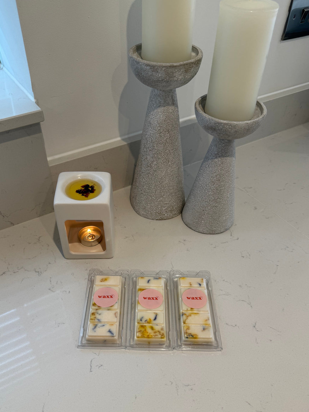 Wax melts and a wax warmer on a white surface with candles in the background.
