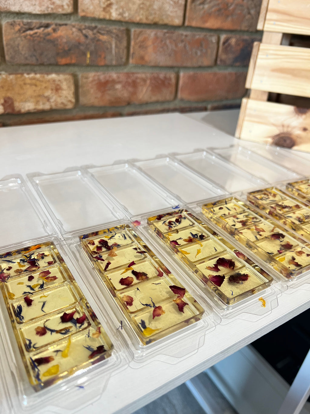 Trays of gold leaf with embedded natural elements on a white surface with a brick wall background.