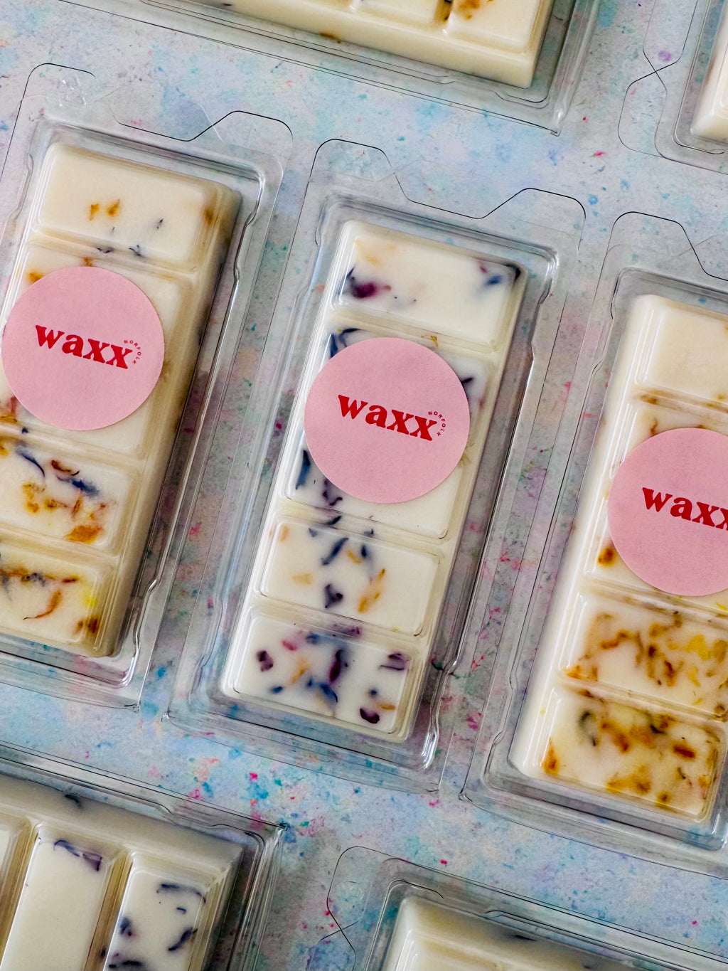 Wax melts in clear packaging with pink 'waxx' label on a patterned surface