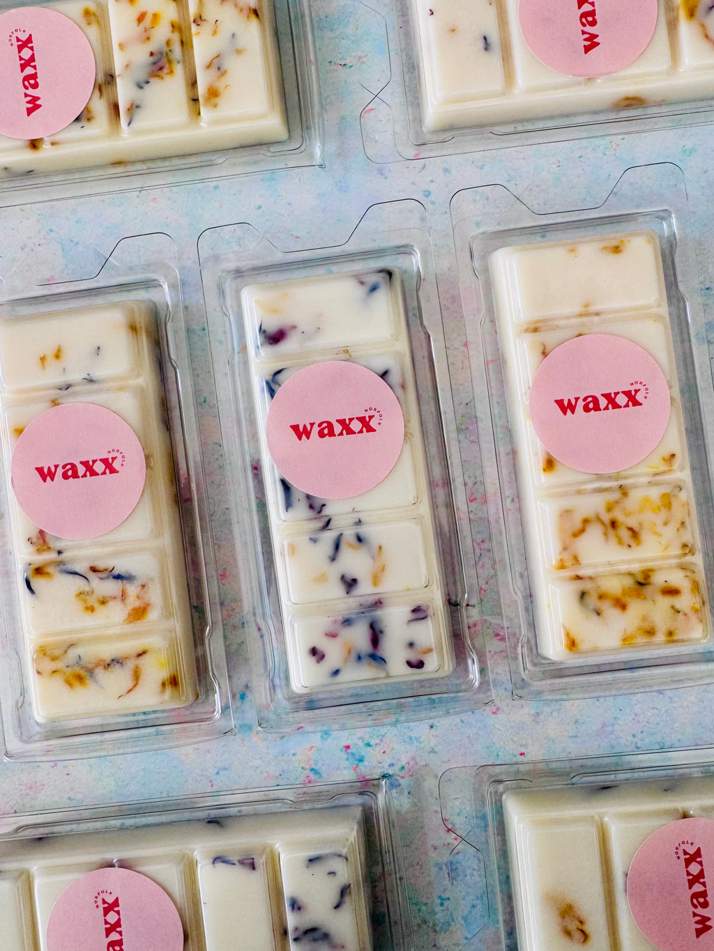 Wax bars in clear packaging with pink 'waxx' labels on a textured surface.