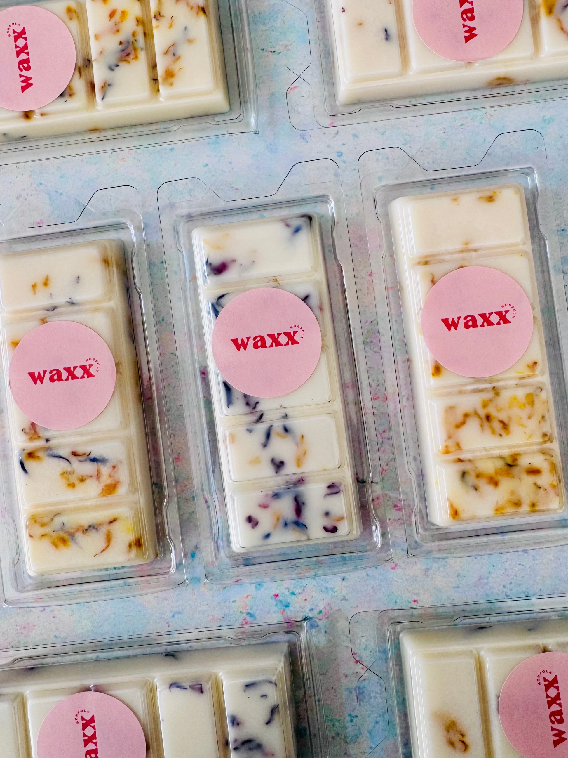 Wax bars in clear packaging with pink 'waxx' labels on a textured surface.