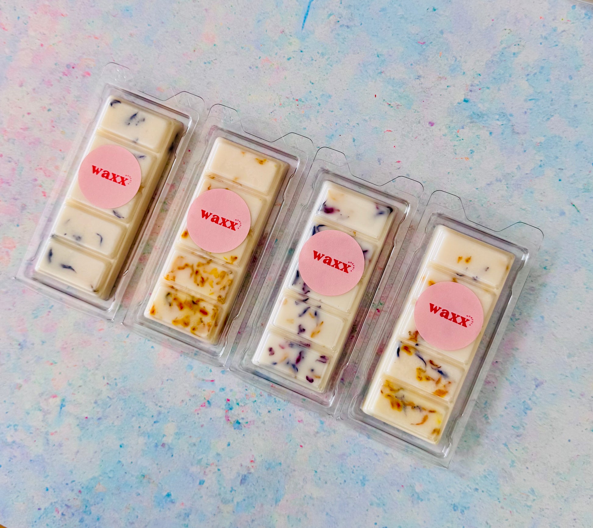 Four wax bars in clear packaging with pink 'waxx' labels on a light blue textured background.